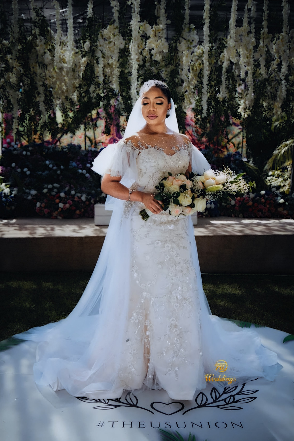 Bride holding her bouquet in front of a floral backdrop