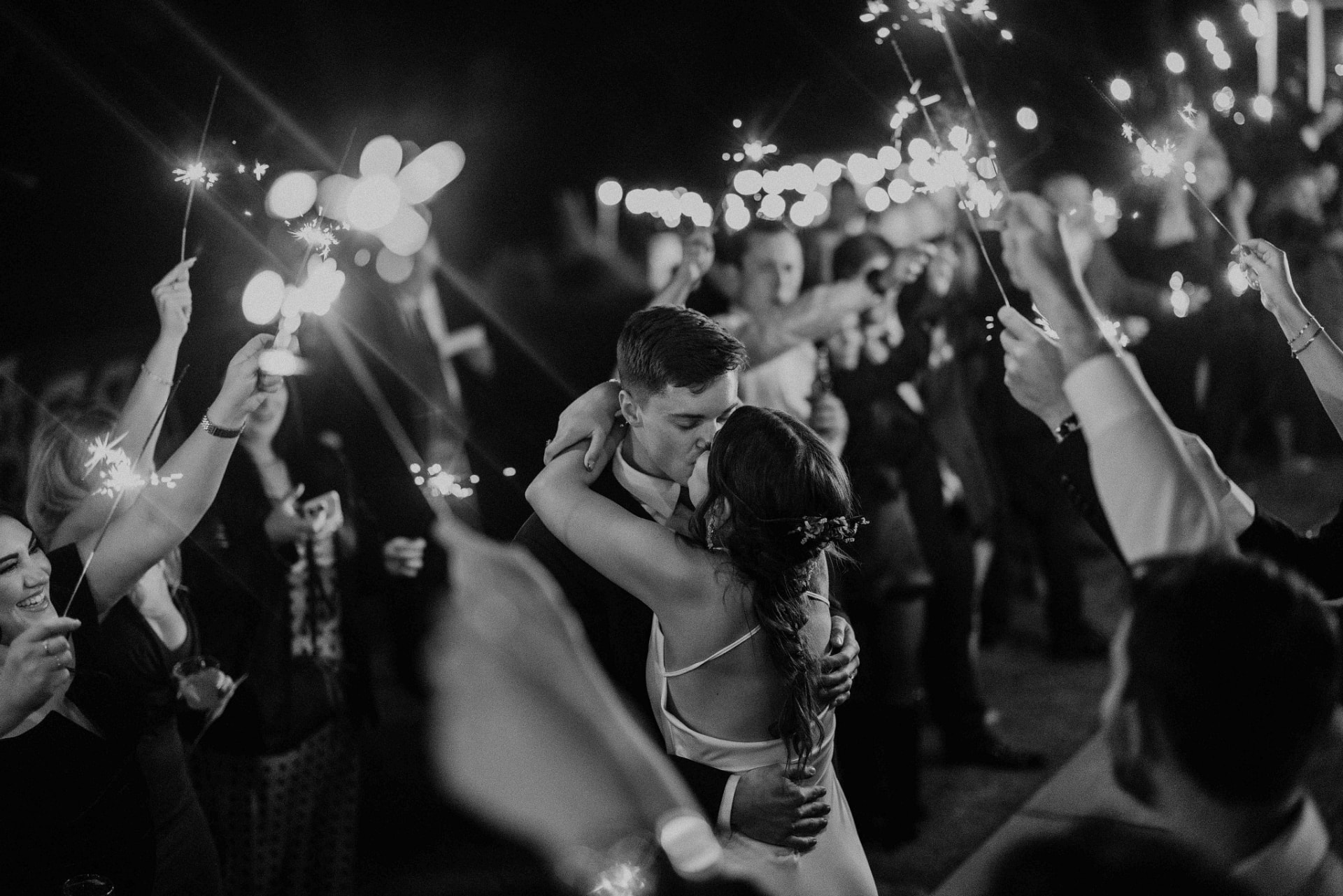 Newlyweds kissing beneath sparklers surrounded by guests