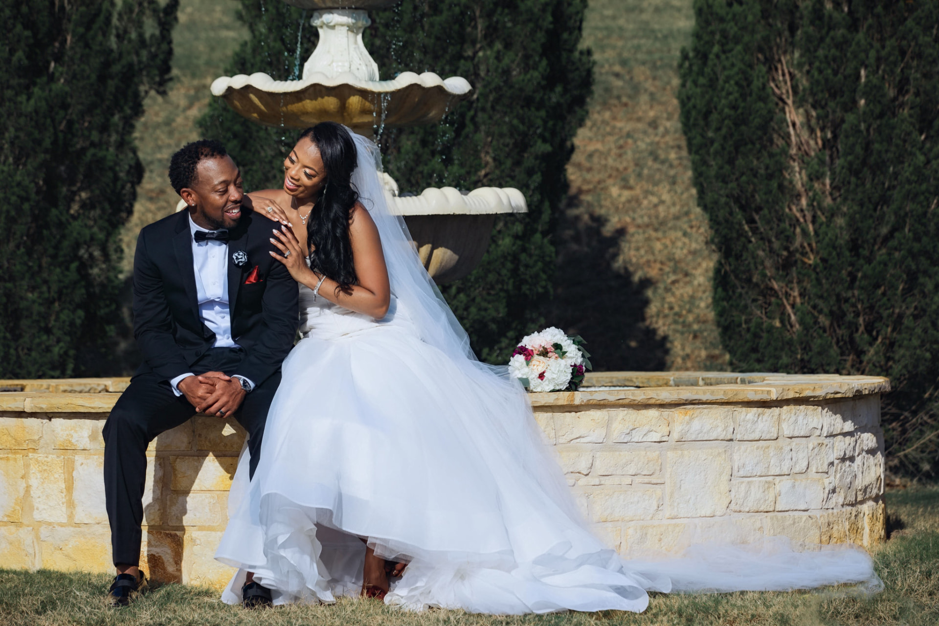 Newlyweds laughing together beside a garden fountain