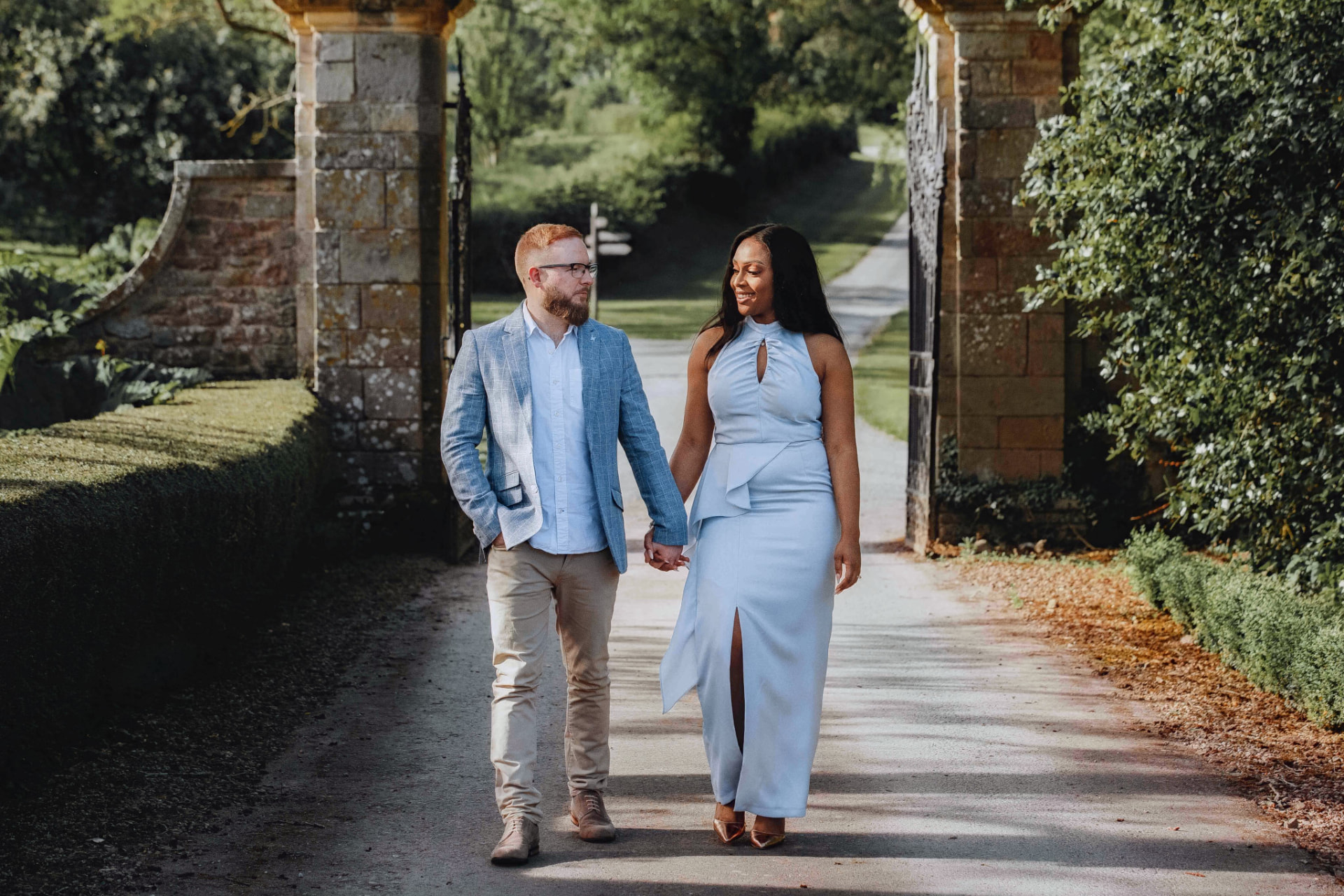 Engaged couple walking hand in hand through a garden