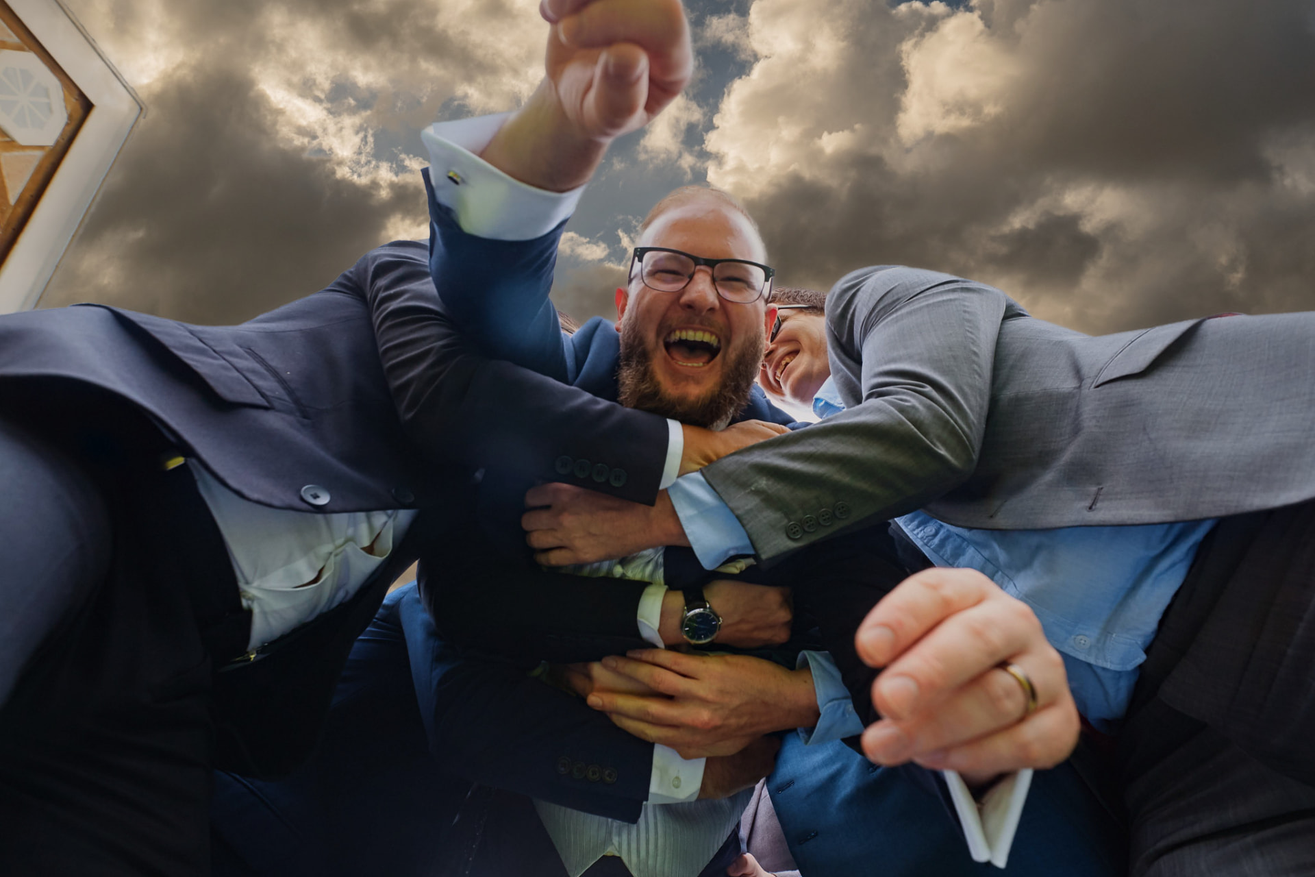 Groom celebrating with his groomsmen under a dramatic sky