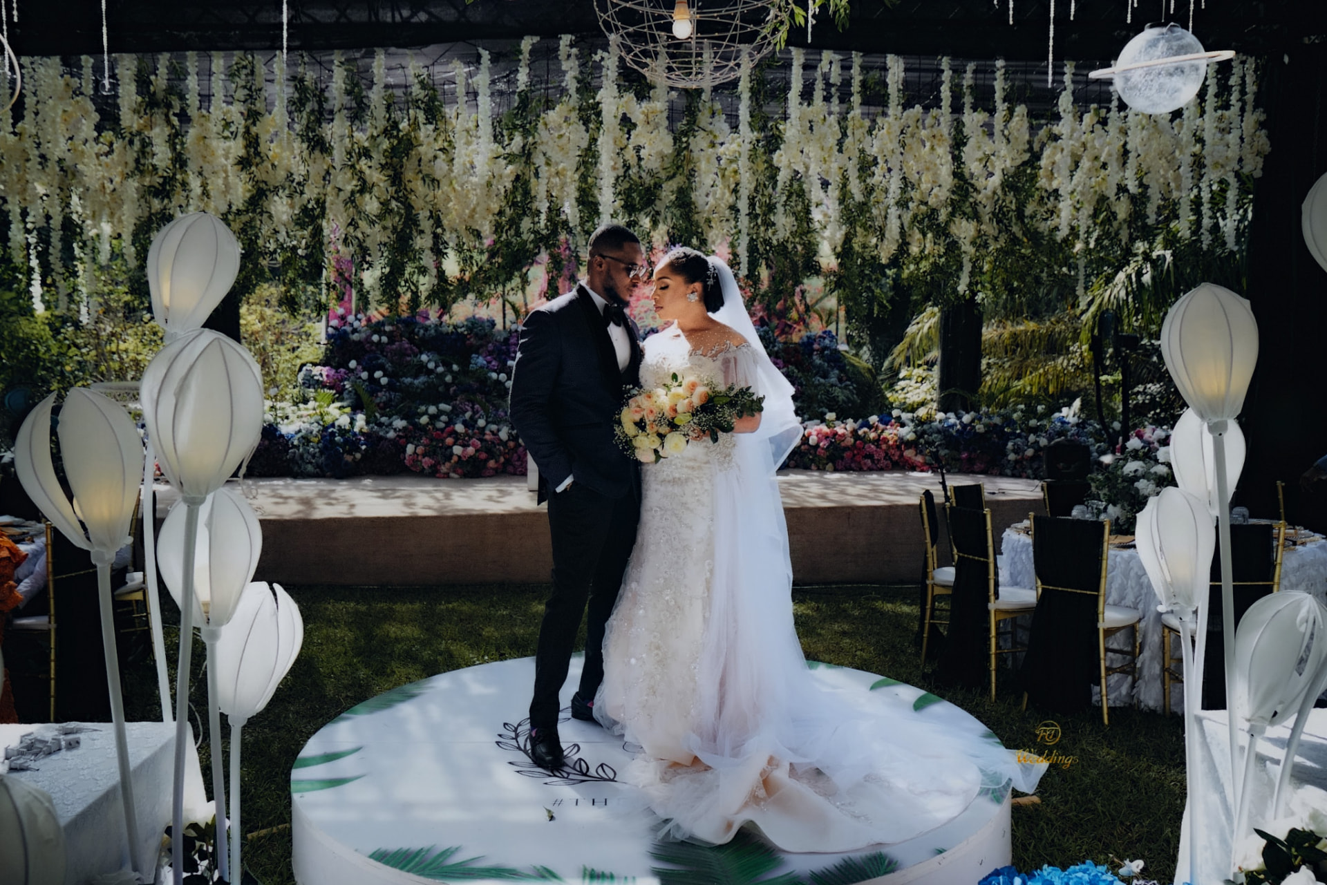 Bride and groom on a floral-draped stage at their reception